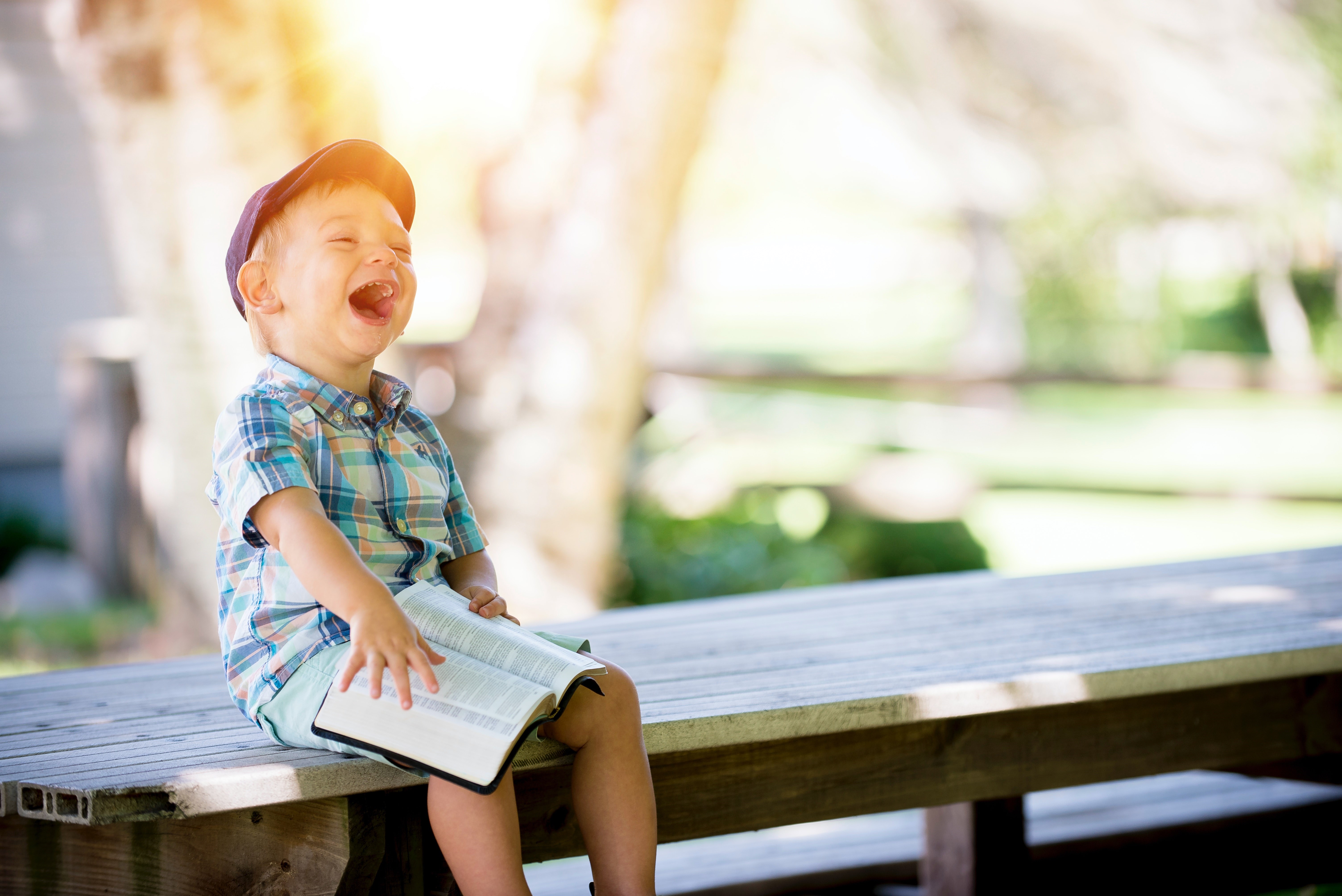 En liten skrattande pojke sitter på en bänk med en bok i knät