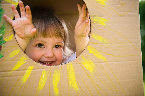 En liten flicka tittar ut genom en kartongbit målad som en sol
