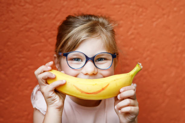 En flicka håller en banan med en ritad glad mun framför ansiktet