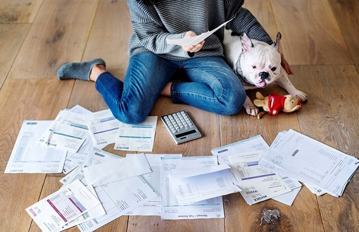 En person och en hund sitter på golvet. Framför dem ligger fakturor utspridda.