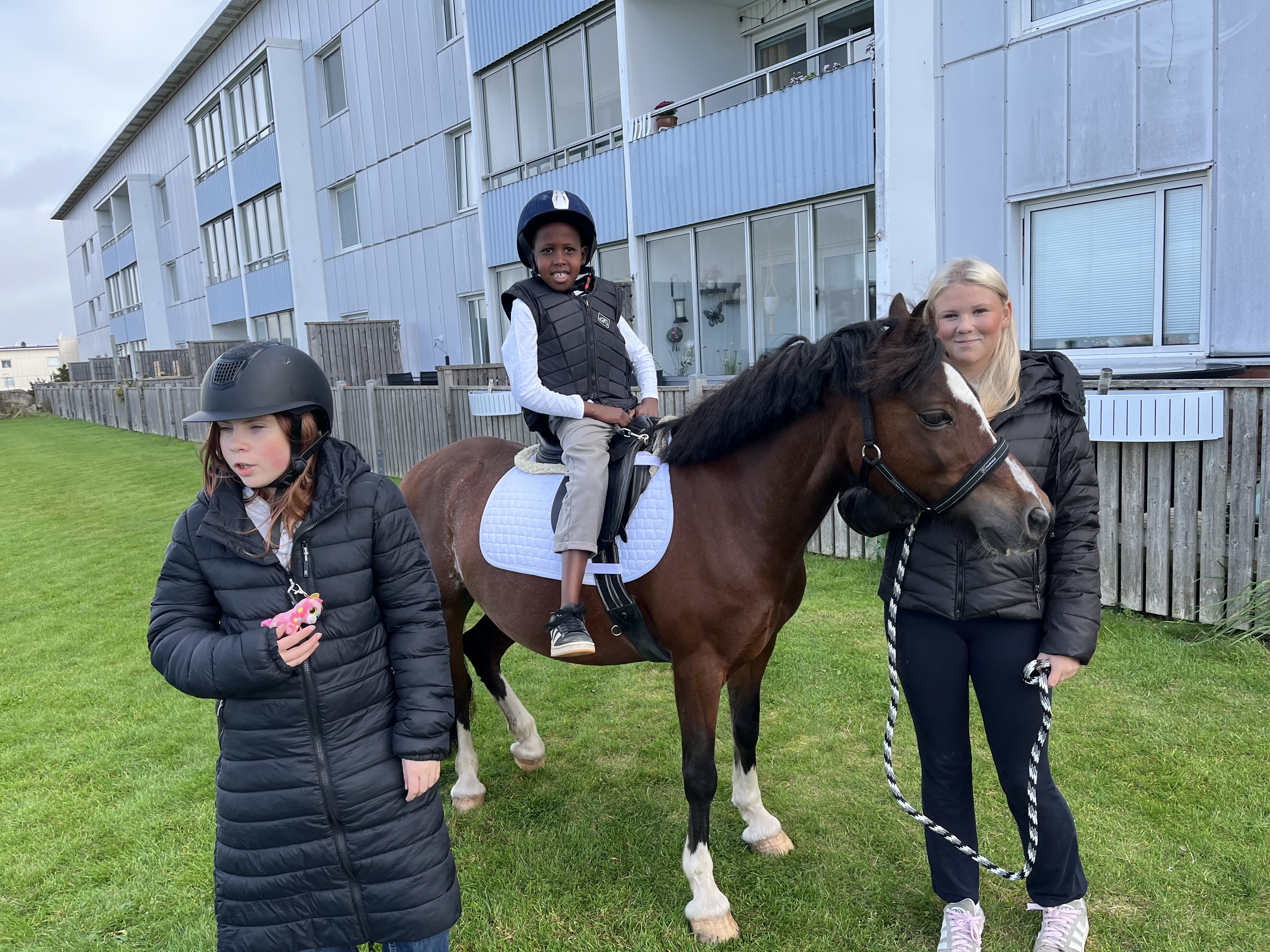 Två tjejer håller i en ponny medan en liten kille sitter på den.