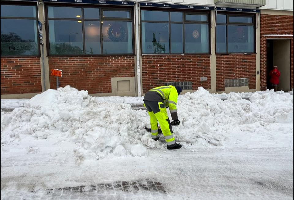 En man klädd i varselkläder skottar snö för hand vid ett övergångsställ.